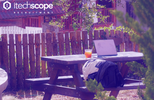 an open laptop on a park bench presumably in a park with an orange drink on the side.
