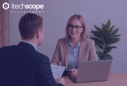 A professional job interview setting with a woman recruiter smiling at a male candidate across the table. She has a laptop open and is holding a tablet, while the candidate holds a resume. The iTechScope Recruitment logo is displayed in the top left corner.
