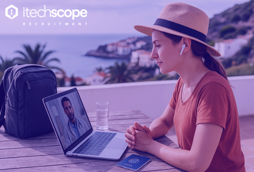 Lady with hat sitting on a balcony with a view of the sea and coastline working on a laptop.